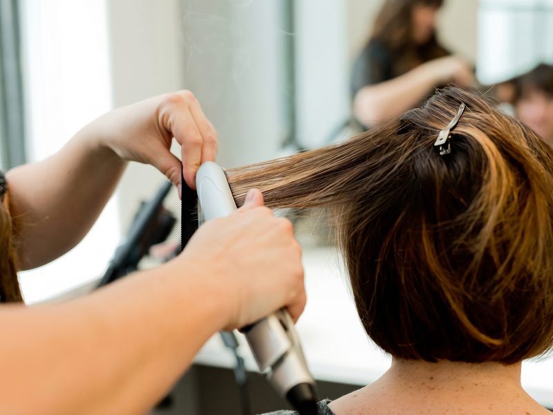 Coiffeuse glättet einer Kundin im Salon die Haare